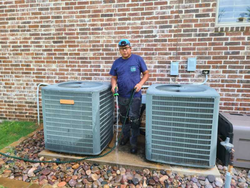 Image of an HVAC maintenance technician washing AC units on a rock base, featuring Comfort Conditioning and highlighting professional HVAC maintenance services.
