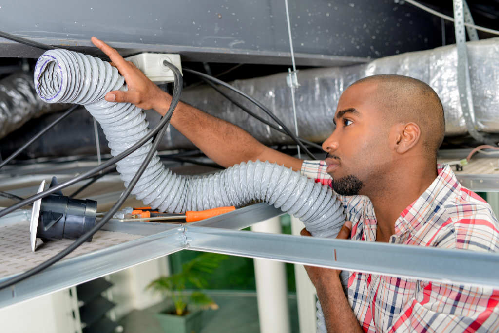 Technician Ductwork Ceiling Install Flexible Vent Image of a technician installing flexible ductwork in a ceiling, featuring Comfort Conditioning and highlighting professional ductwork installation services.